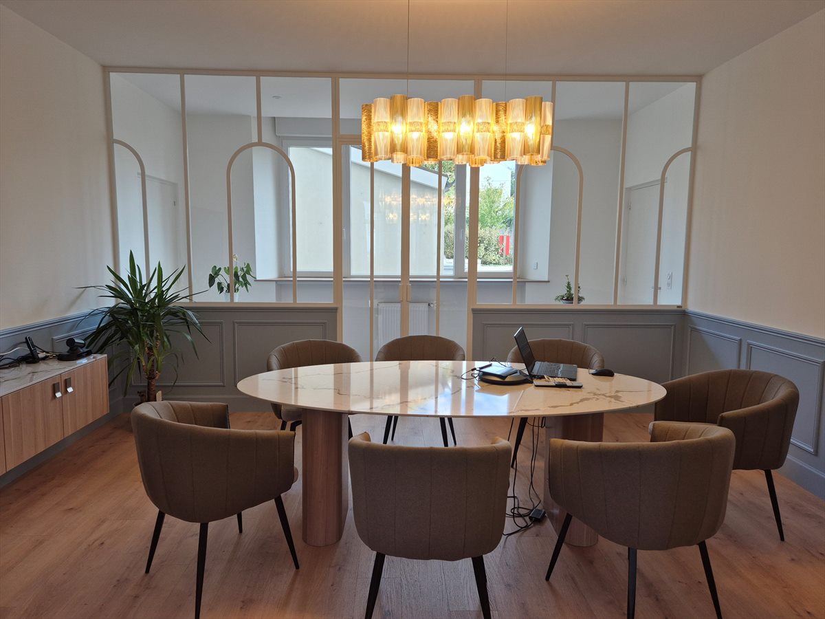 La salle de signature de l'étude : table ovale en marbre blanc entourée de fauteuils, suspension dorée et verrière